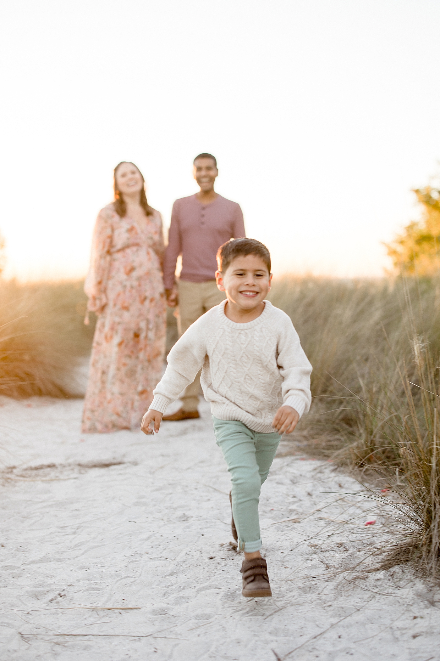 Boy running along the sand while Mom and Dad look after him. Family photos by Brittany Elise Photography.