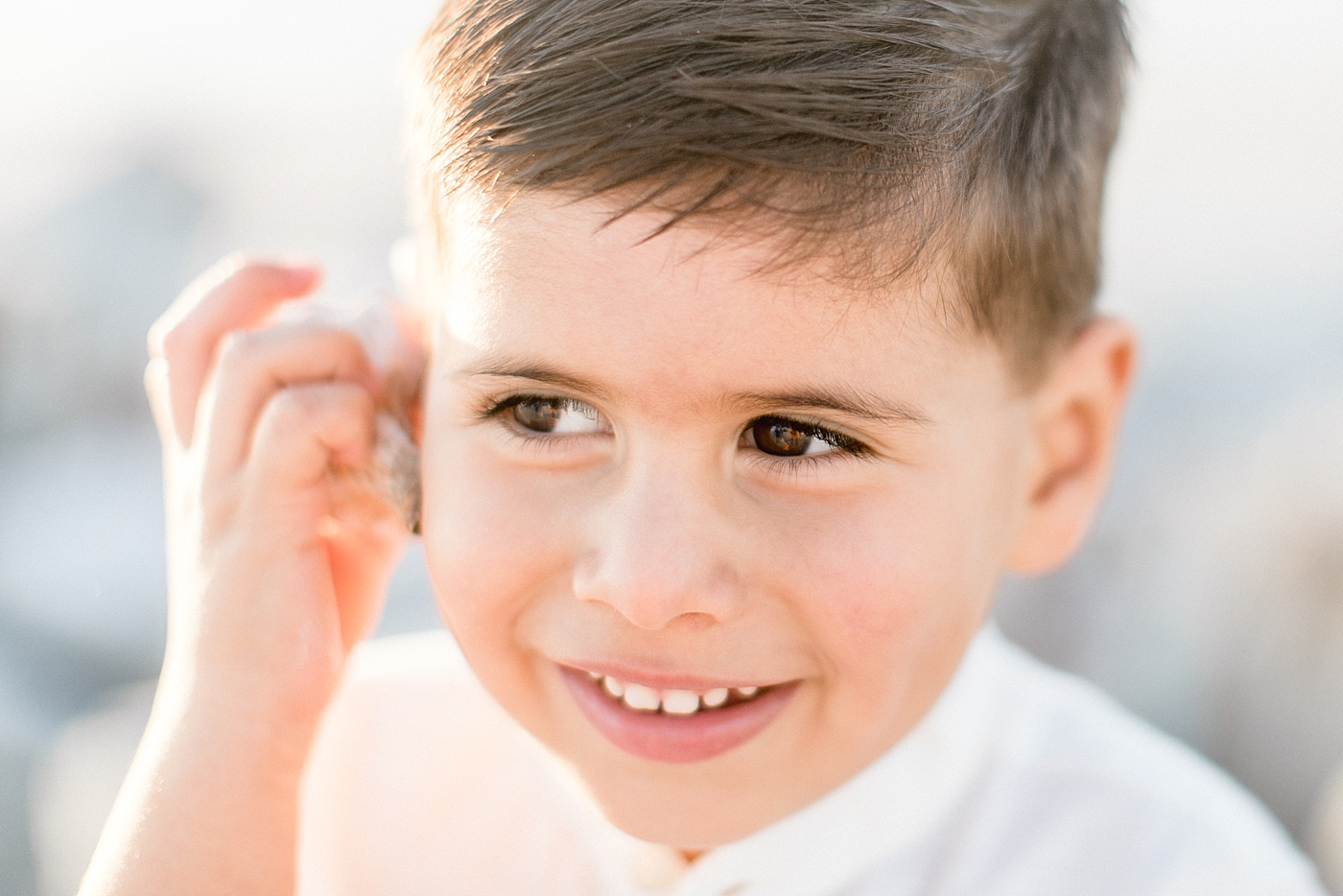 Young boy with seashell up to his ear while playing on the beach | Brittany Elise Photography