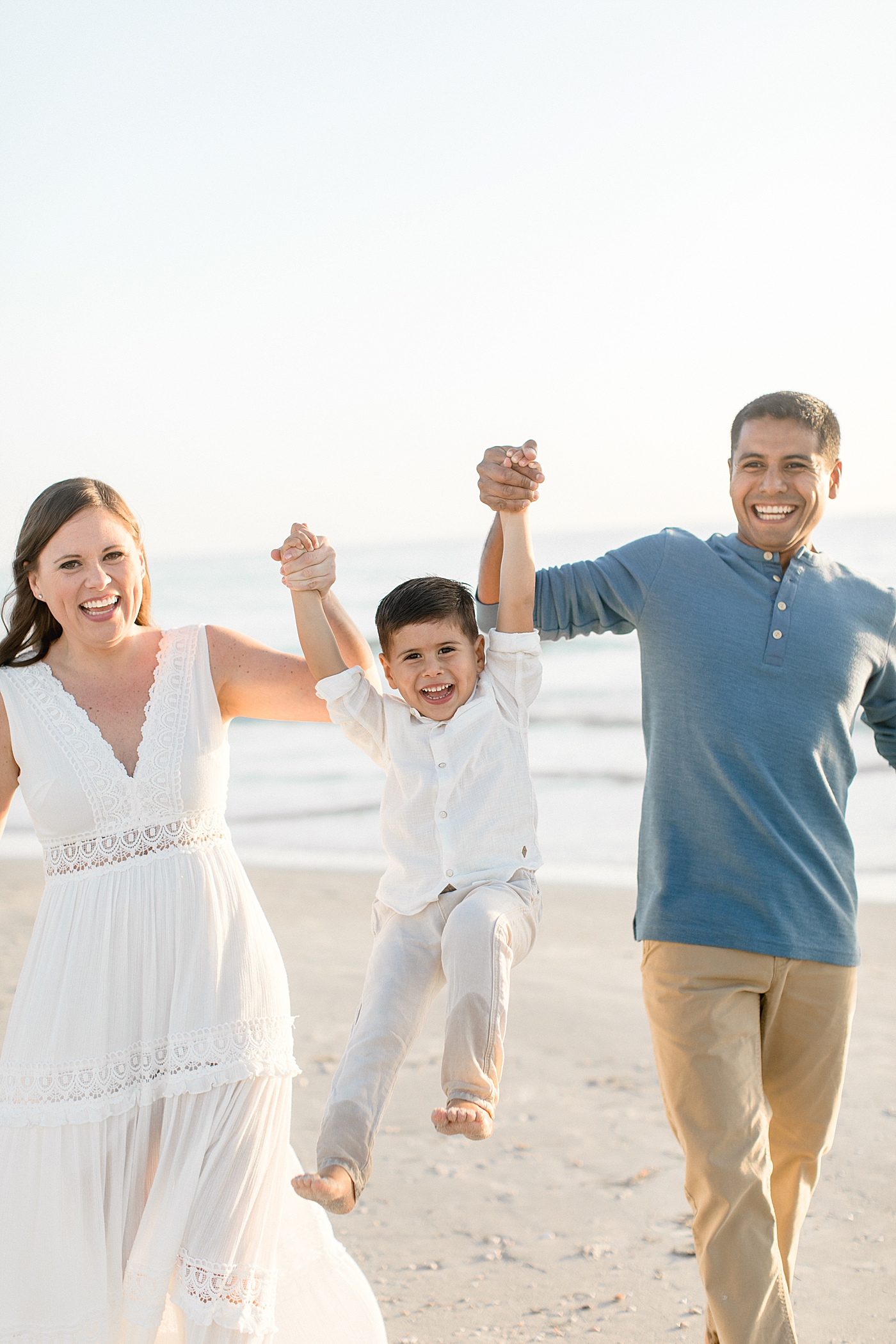 Mom and Dad swinging their son on the beach. Everyone has big smiles on their face. Photos by Brittany Elise Photography.