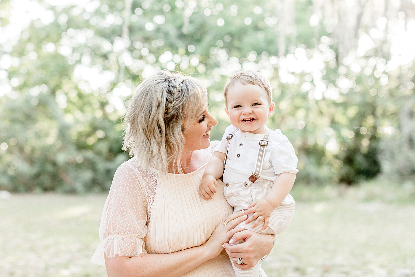 Mom is looking at one year old son that's smiling so big! Photo by Brittany Elise Photography.