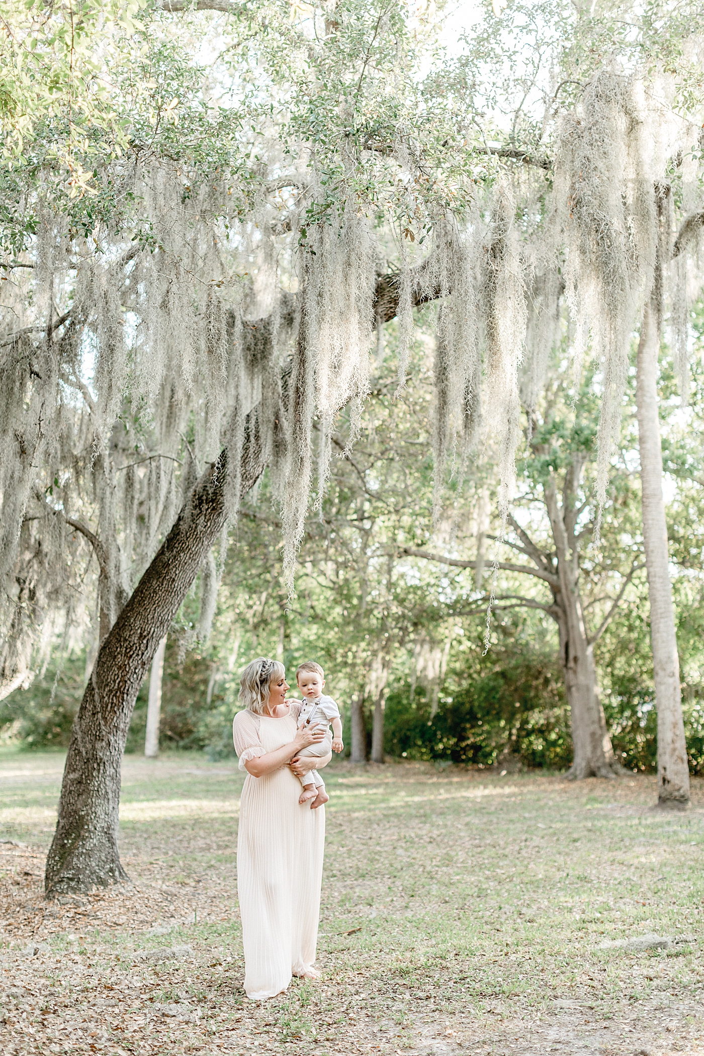 Mom is holding her son walking under the oak trees. Photo by Brittany Elise Photography.