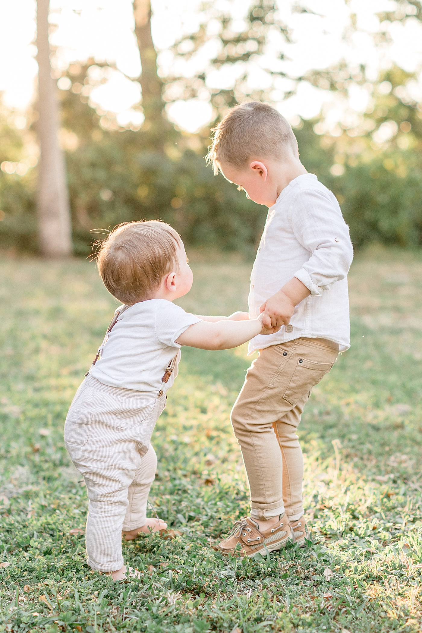 Brothers holding hands and playing in the field. Photo by Brittany Elise Photography.