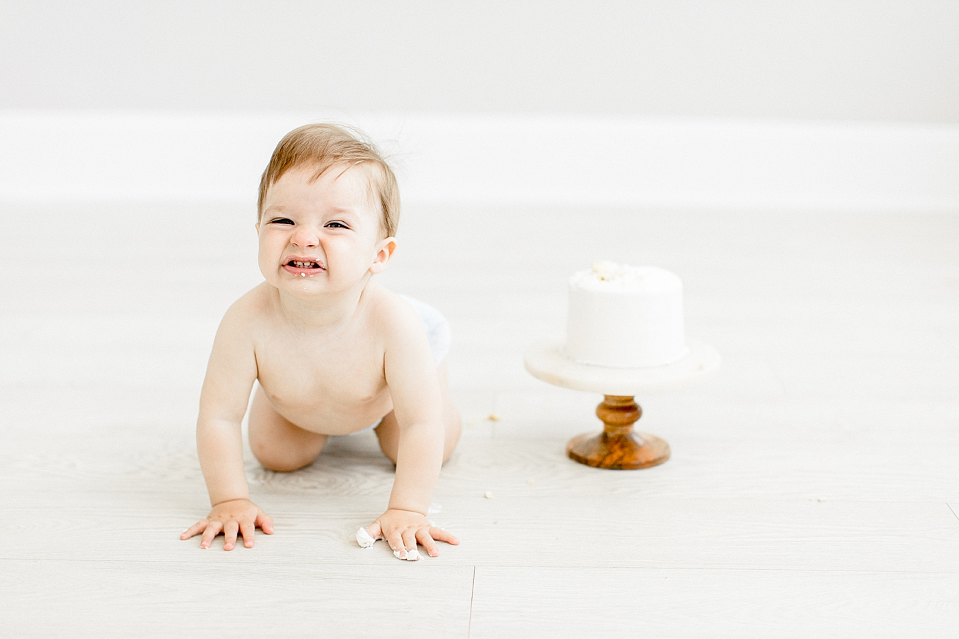 One year old crawling away from cake during cake smash photoshoot. Photo by Brittany Elise Photography.