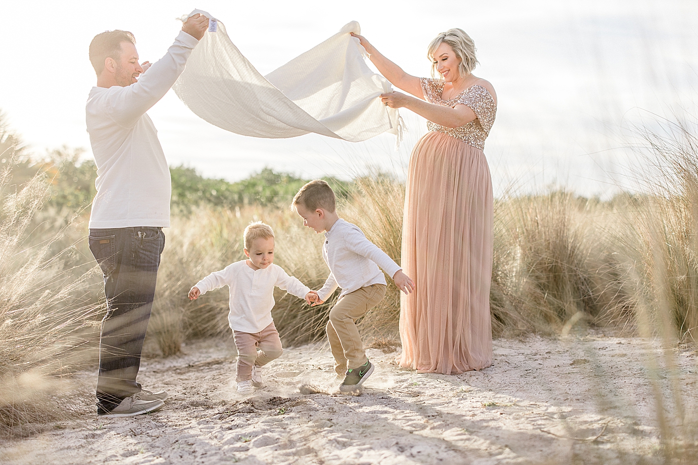 Two boys running under blanket Mom and Dad are holding. Sun is setting behind them. Photo by Brittany Elise Photography.