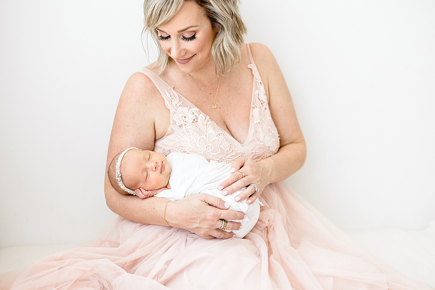 Mom in beautiful pink, lace dress looking at her newborn baby girl. Photo by Brittany Elise Photography.