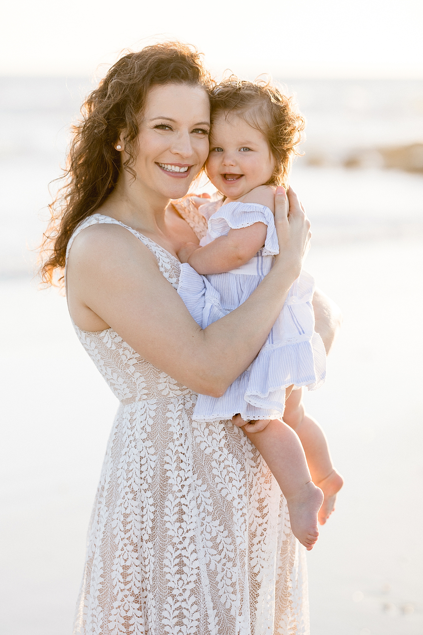 Mom holding baby girl on the beach for sunset photos. Photo by Brittany Elise Photography.