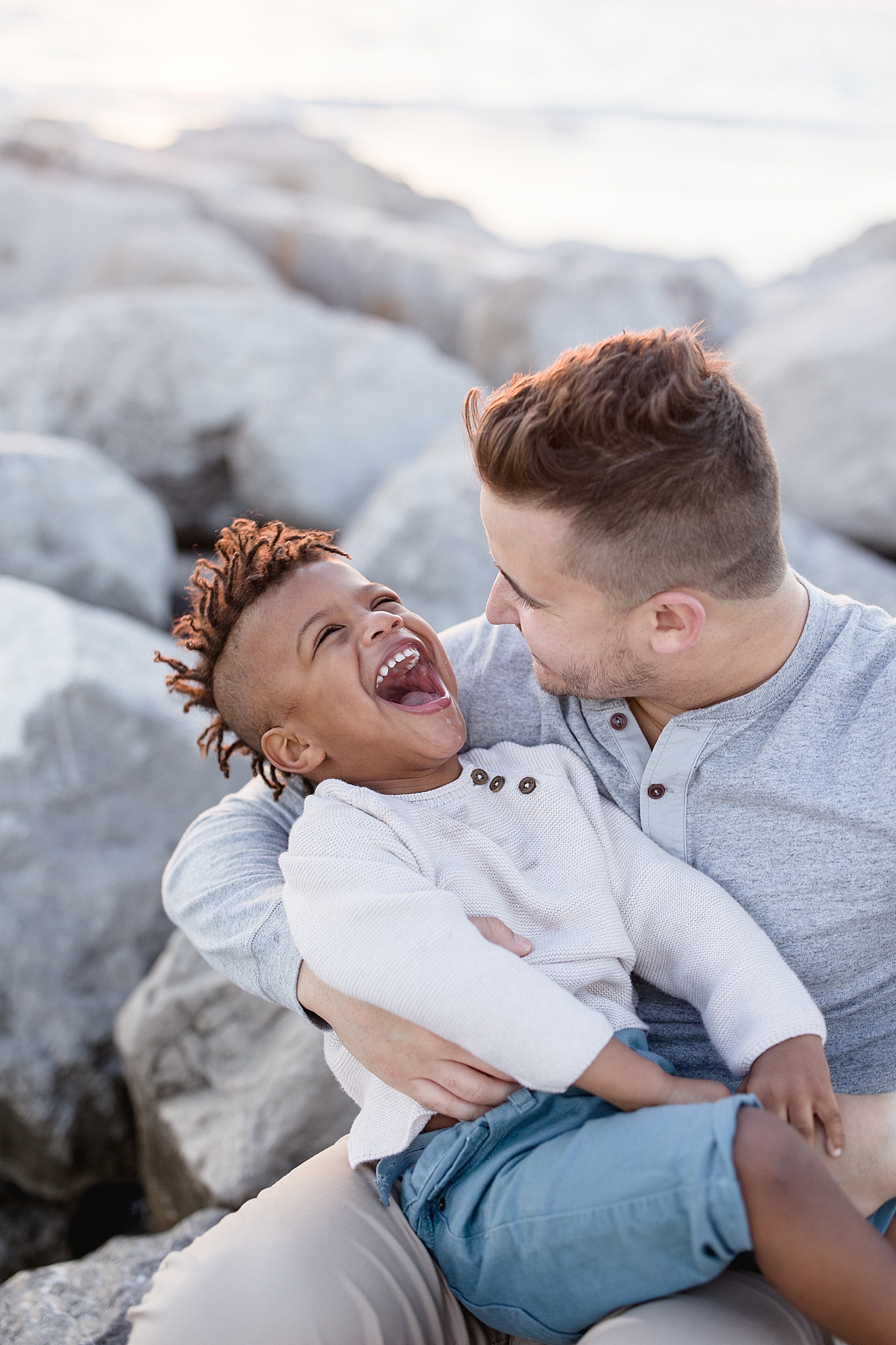 Dad holding his son while sitting on the rocks at St. Pete Beach. Photo by Brittany Elise Photography.