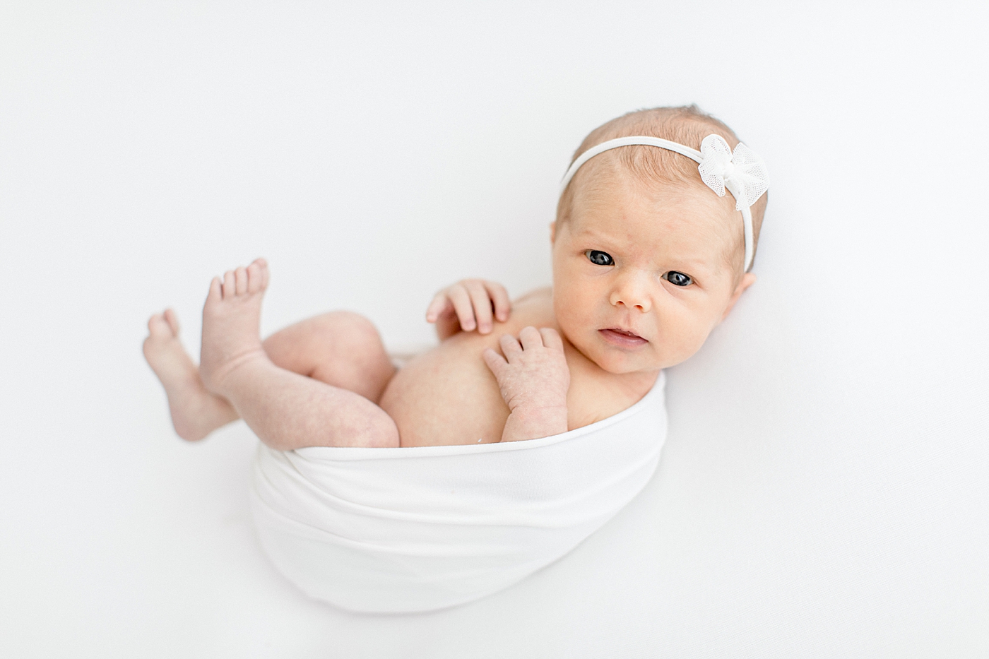 Baby girl wide awake and swaddled in white for newborn photos. Photo by Brittany Elise Photography.