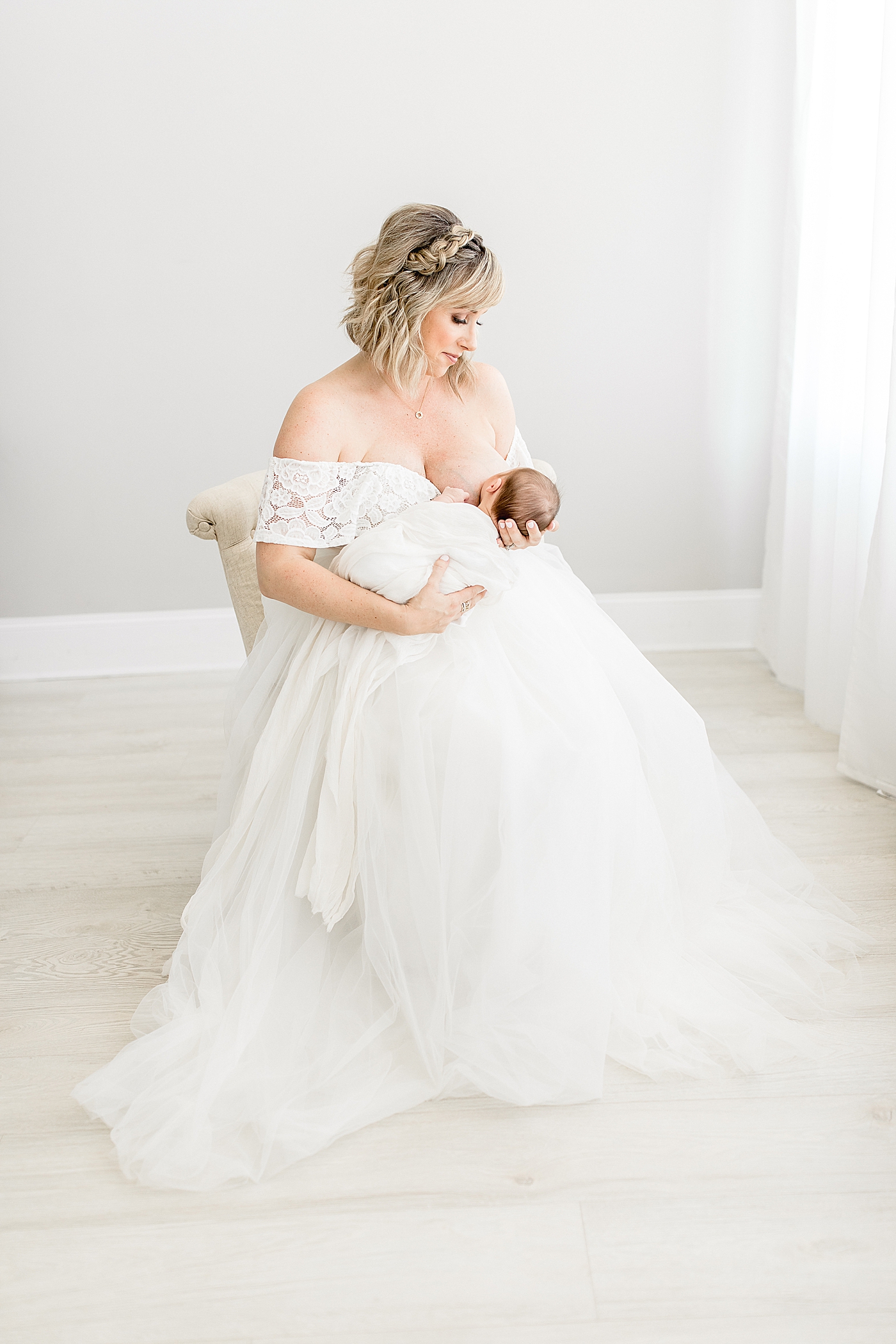 Mom in beautiful tulle white dress nursing her newborn. Photo by Brittany Elise Photography.