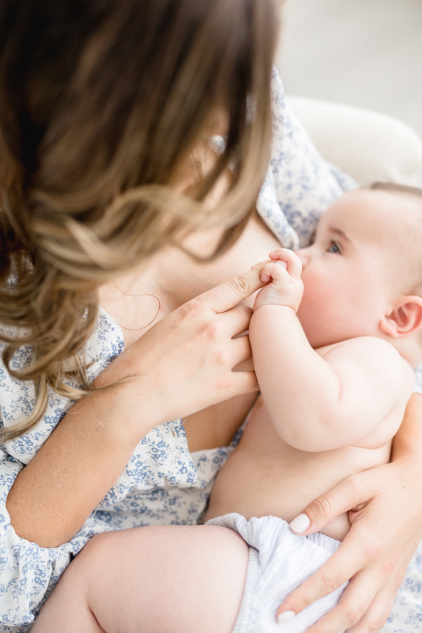 Mom breastfeeding baby while he holds onto her finger. Photo by Brittany Elise Photography.