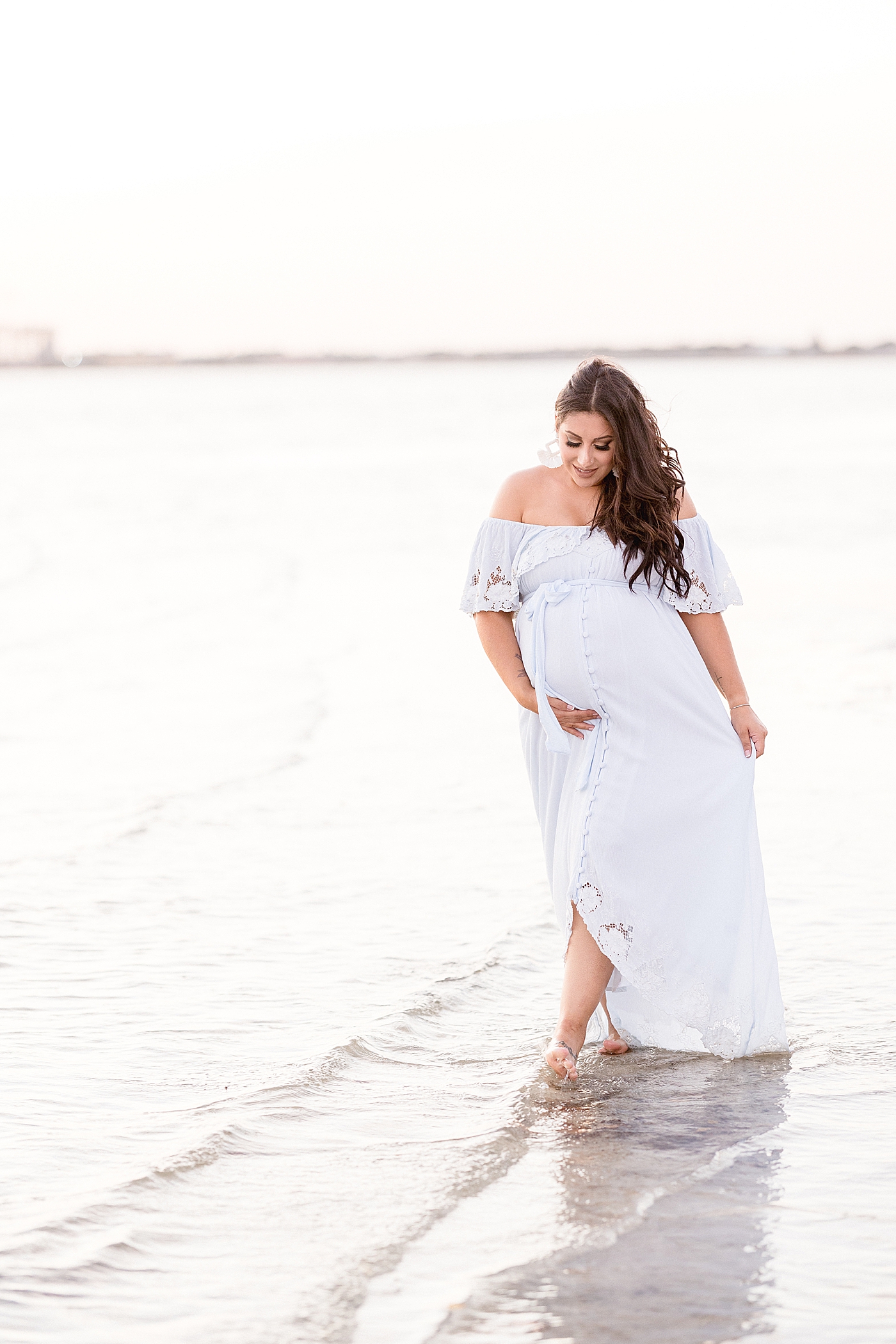 Mom walking along water at the beach in blue Fillyboo maternity dress. Photo by Brittany Elise Photography.