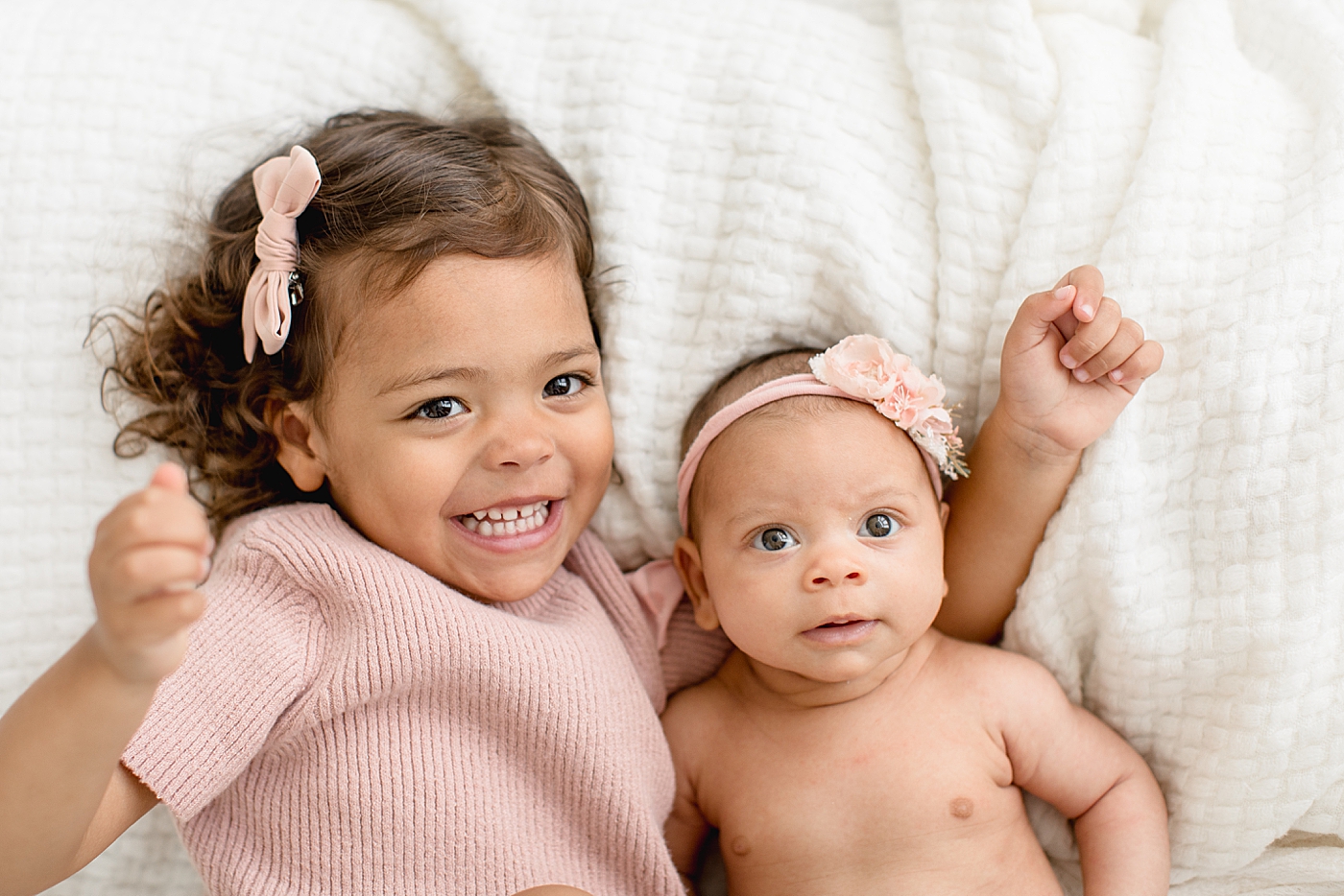 Sisters laying beside each other for baby sisters newborn photos. Photo by Brittany Elise Photography.