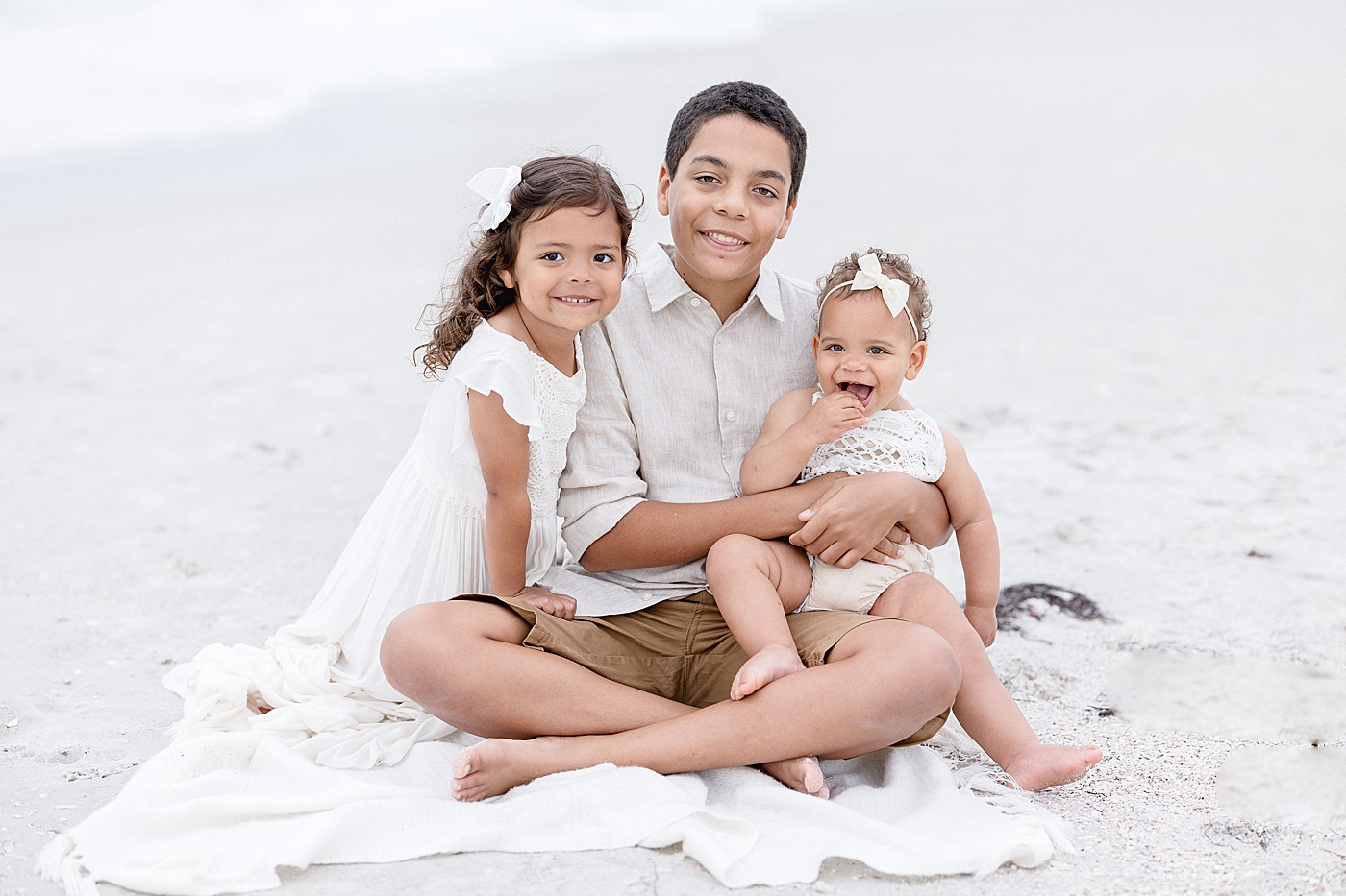 Siblings sitting on the beach during family photos. Photo by Brittany Elise Photography.