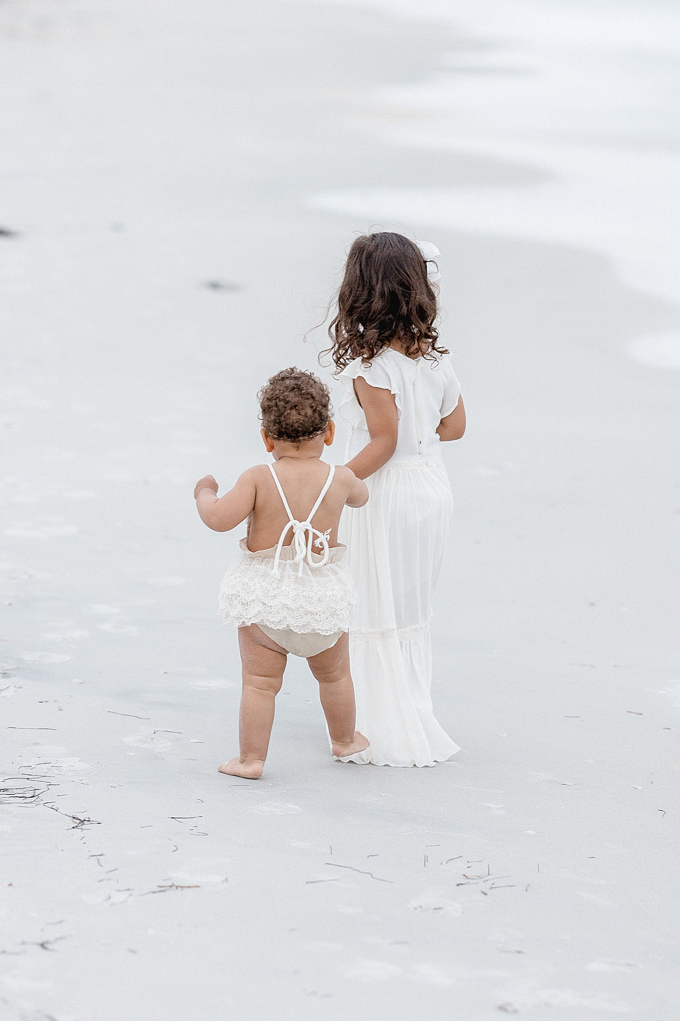 Sisters holding hands walking on the beach. Photo by Brittany Elise Photography.