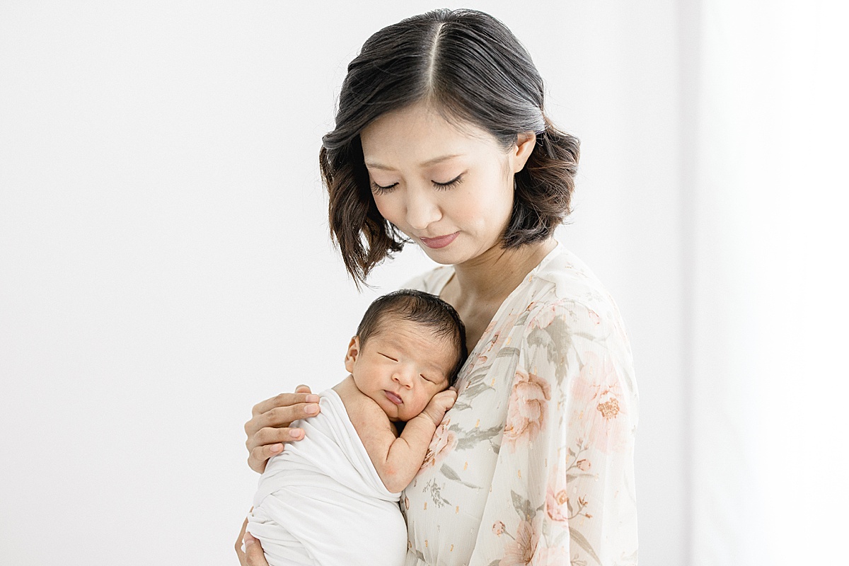 Mom wearing floral dress holding newborn son. Photo by Brittany Elise Photography.