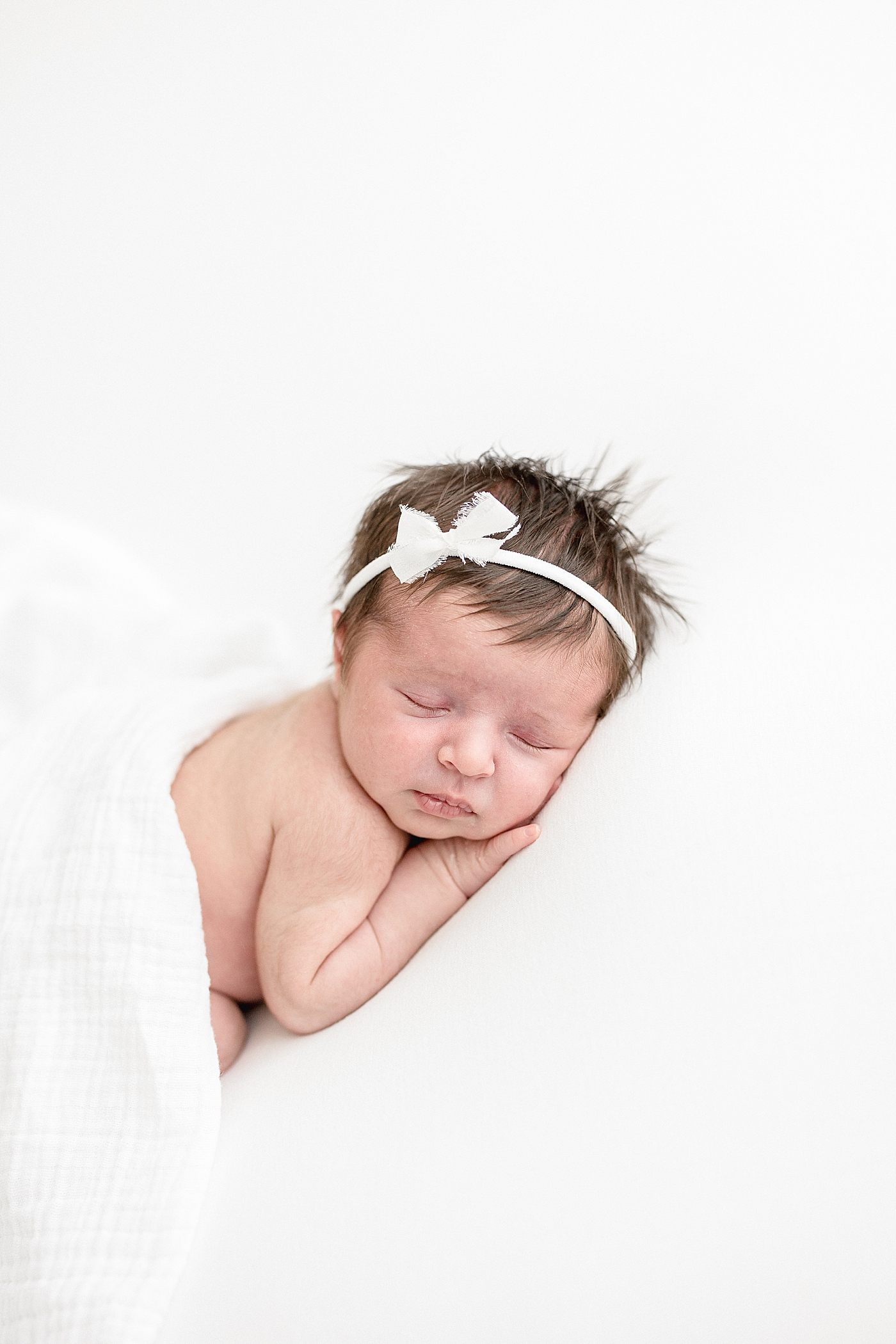 Baby girl sleeping on her stomach with white bow and blanket. Photos by Brittany Elise Photography.