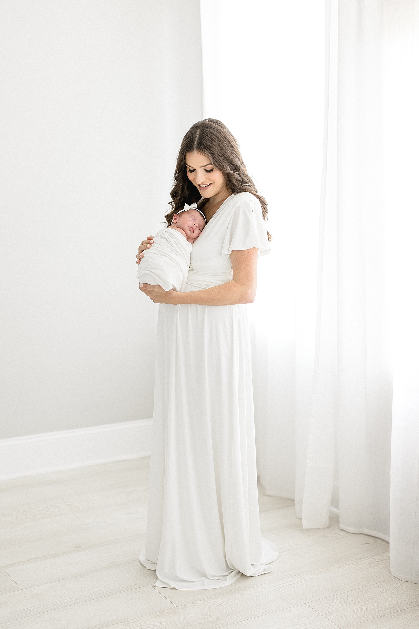 Mom in a long white dress holding her newborn daughter. Photo by Brittany Elise Photography.