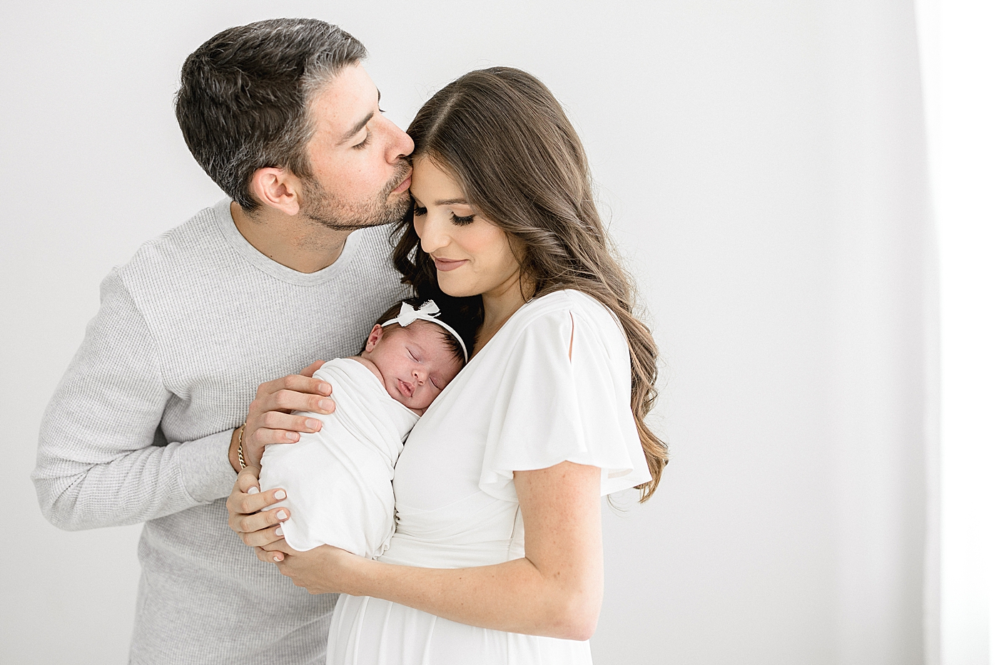 Dad giving Mom a kiss while she's holding their baby girl. Photos by Brittany Elise Photography.