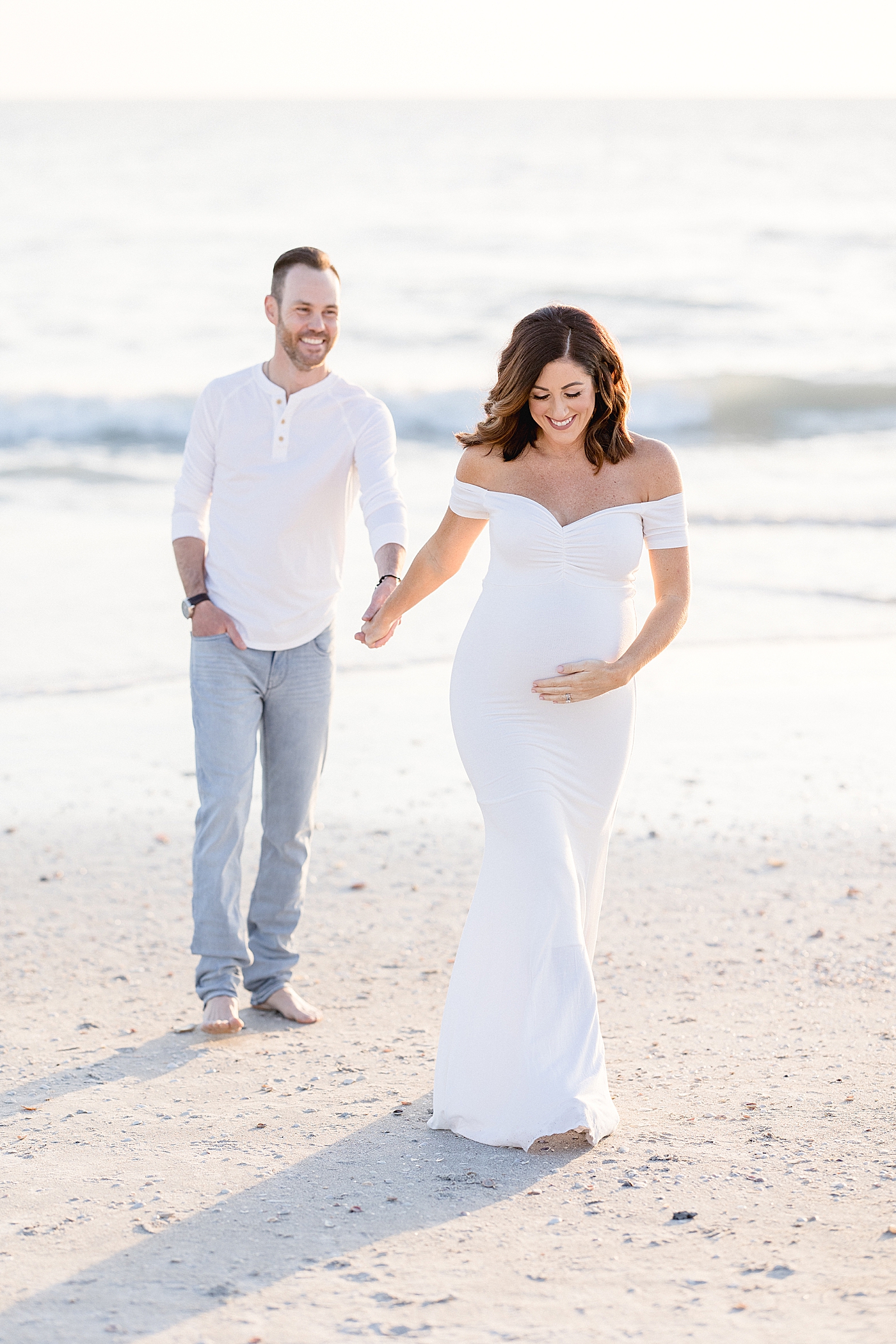 Expecting parents walking on the beach at sunset. Photo by Brittany Elise Photography.