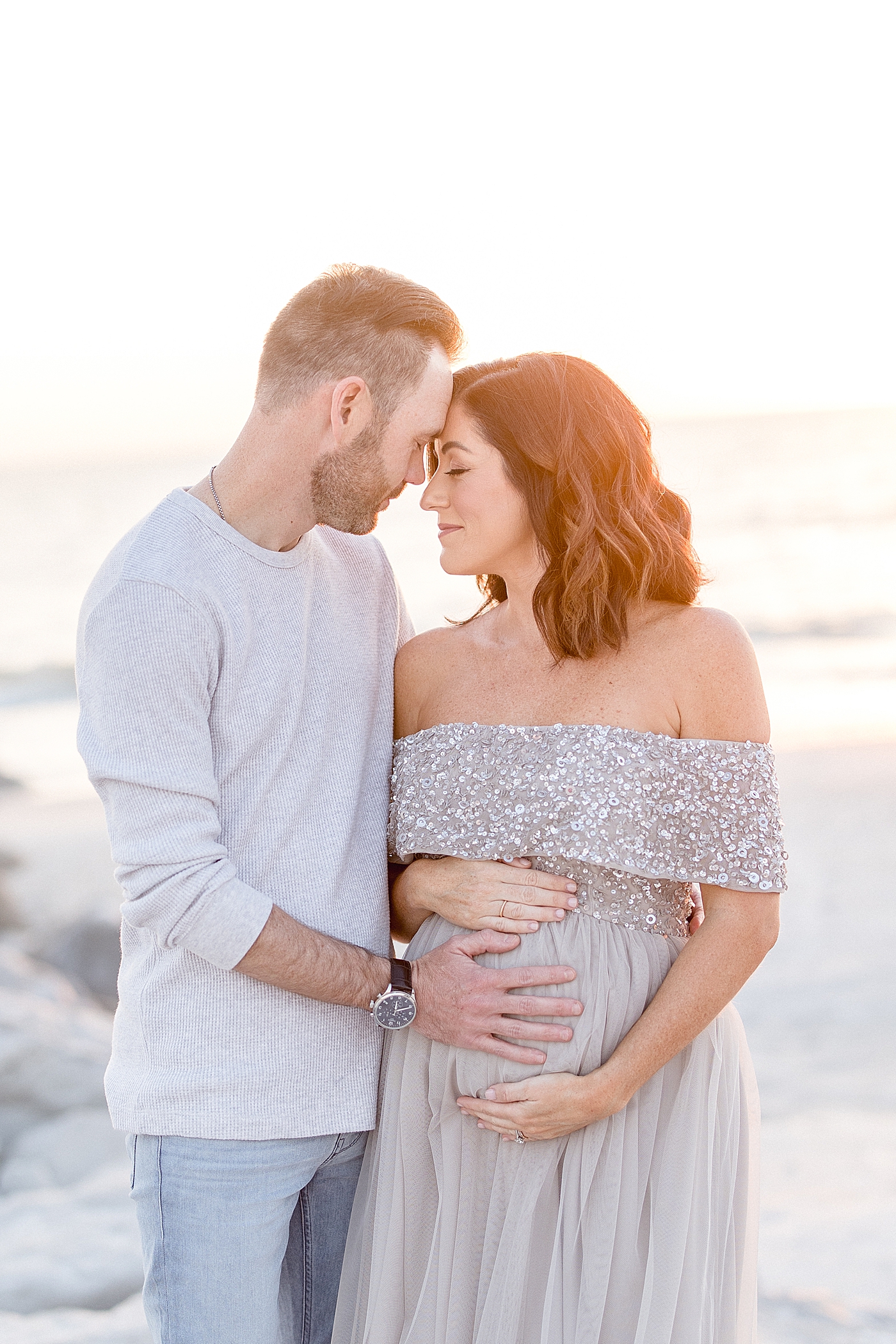 Expecting parents with heads together on the beach. Photo by Brittany Elise Photography.