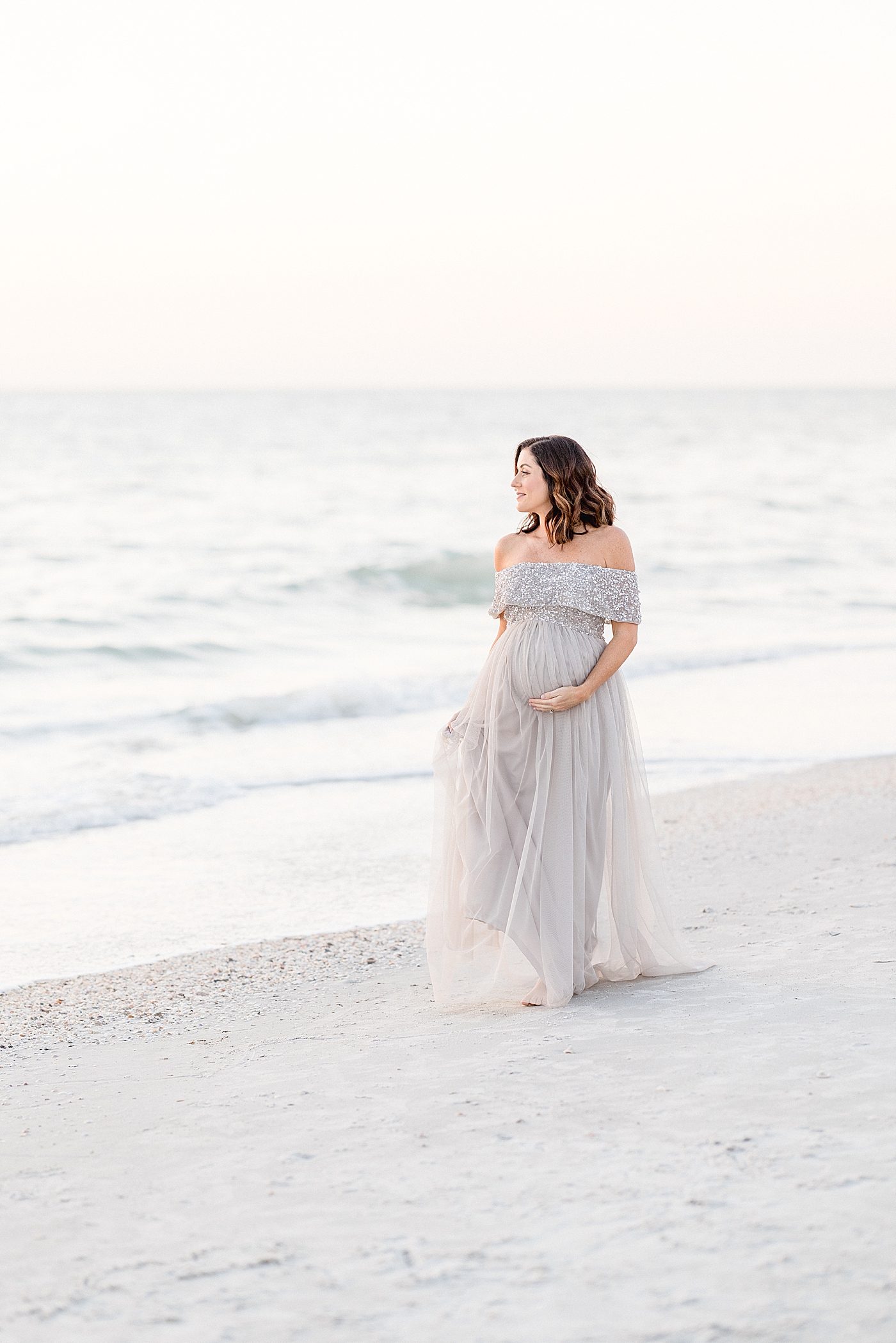 Expecting mom walking along the beach. Photo by Brittany Elise Photography.