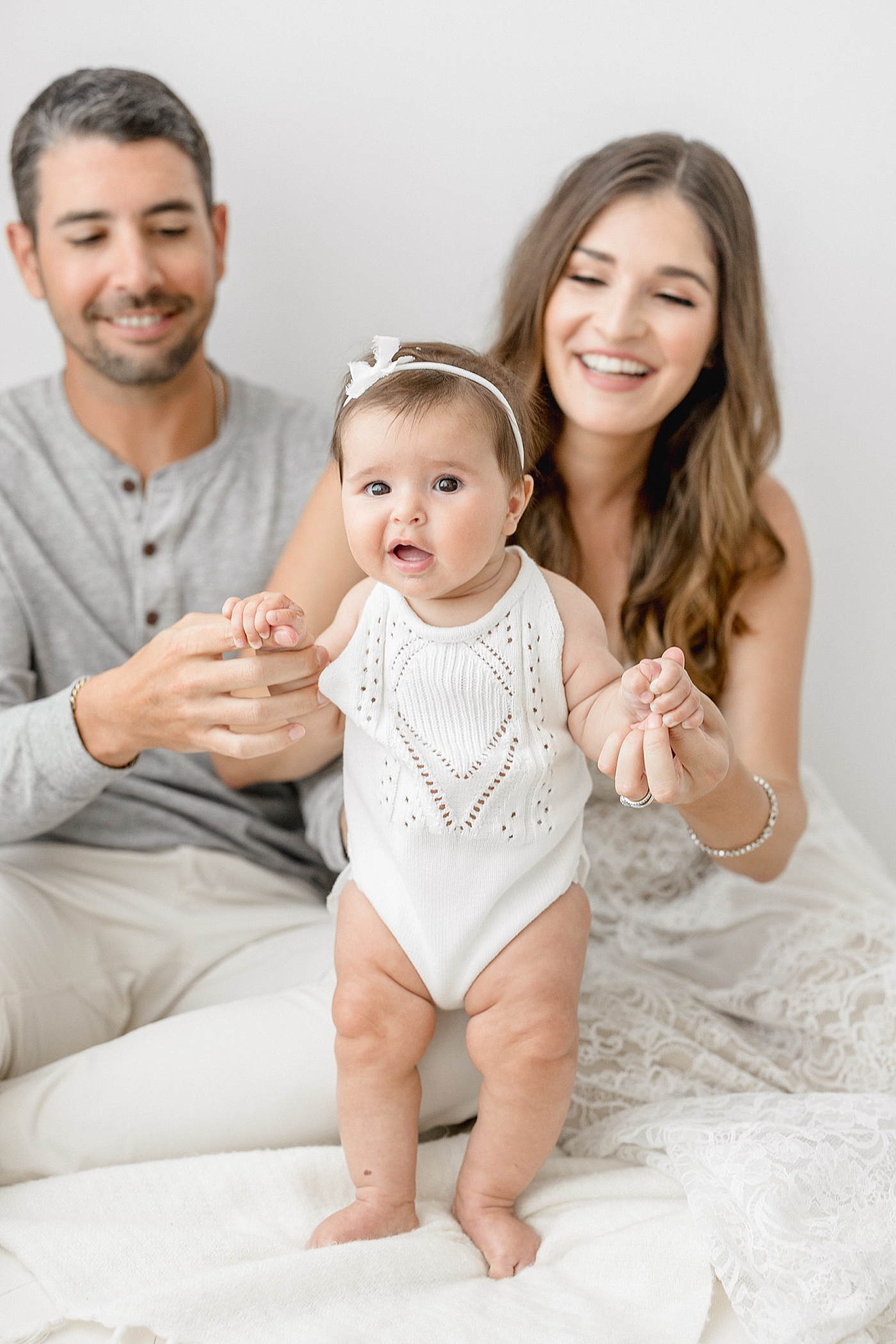 Six month old baby standing with support from Mom and Dad. Photos by Brittany Elise Photography.