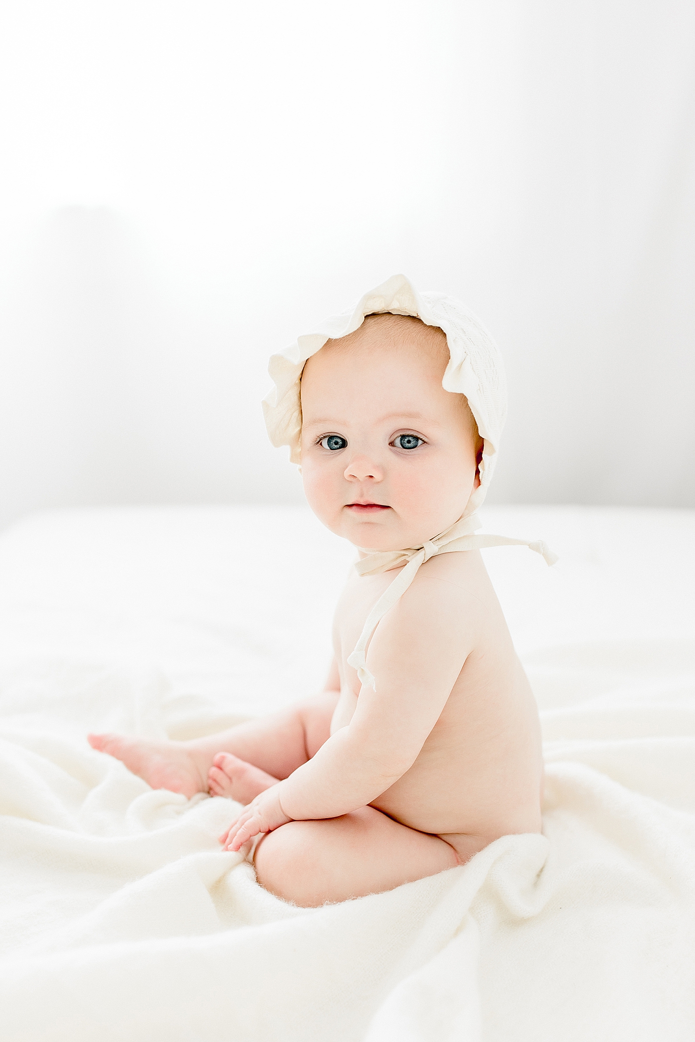 Six month old baby girl sitting with a bonnet on. Photo by Brittany Elise Photography.