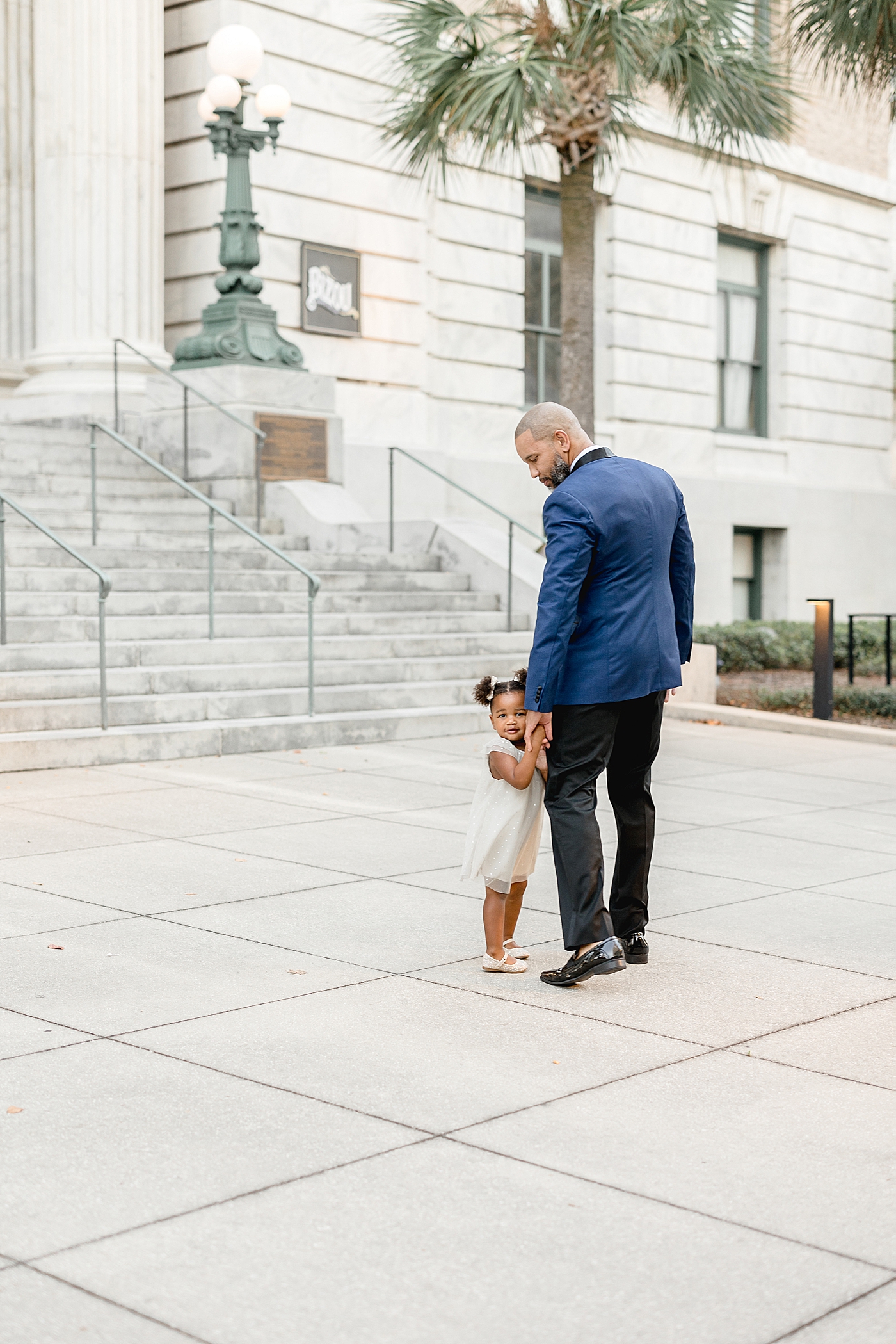 Two year old little girl holding her Dad's hands walking. Photos by Brittany Elise Photography.