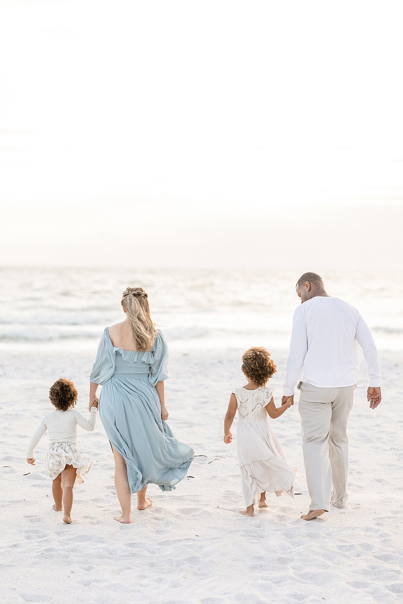 Family of four walking on the beach towards the water at sunset. Photo by Brittany Elise Photography.