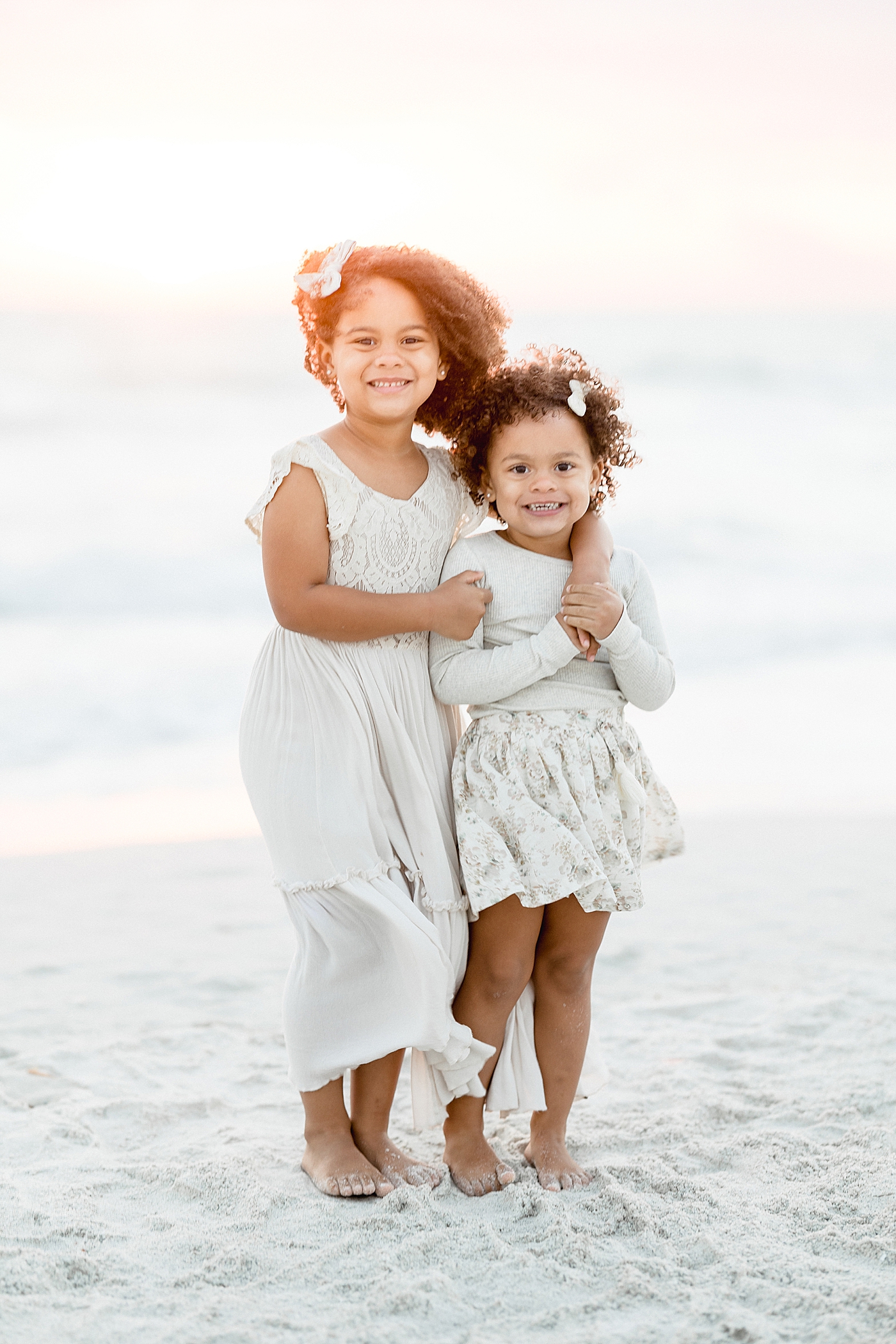 Sisters standing together with arms around each other on the beach. Photo by Brittany Elise Photography.
