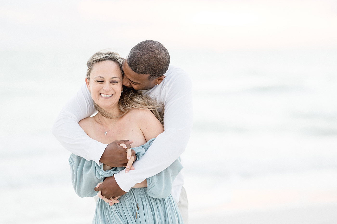 Husband embracing his wife with a hug on the beach. Photo by Brittany Elise Photography.