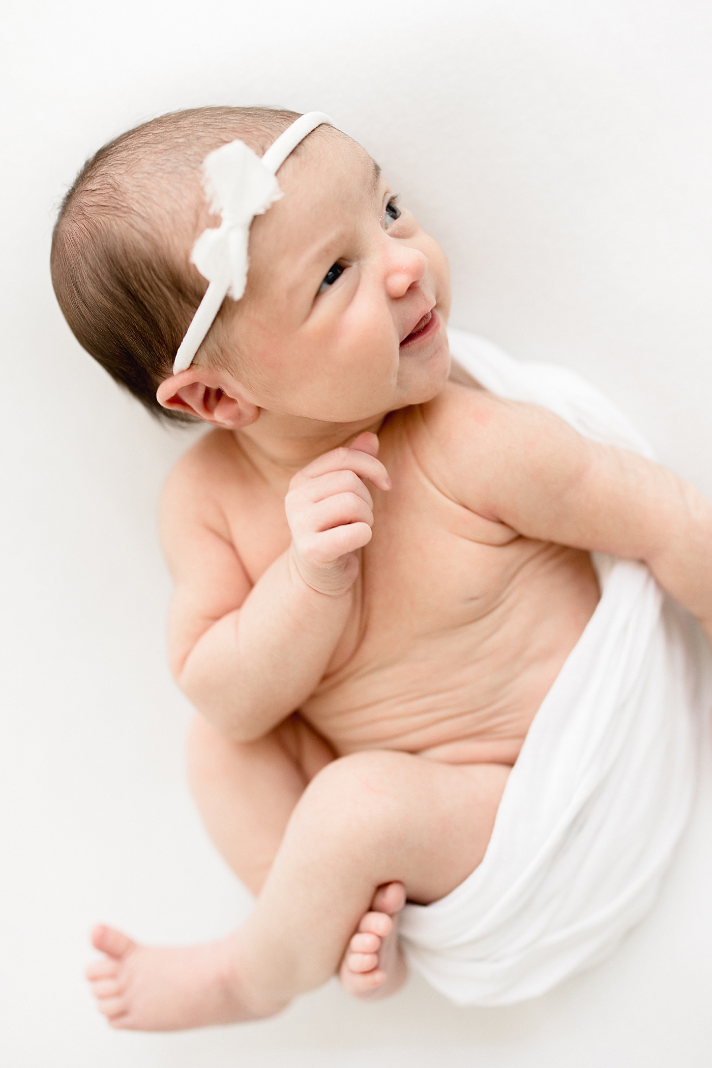 Baby girl swaddled in white blanket with white headband. Photo by Brittany Elise Photography.