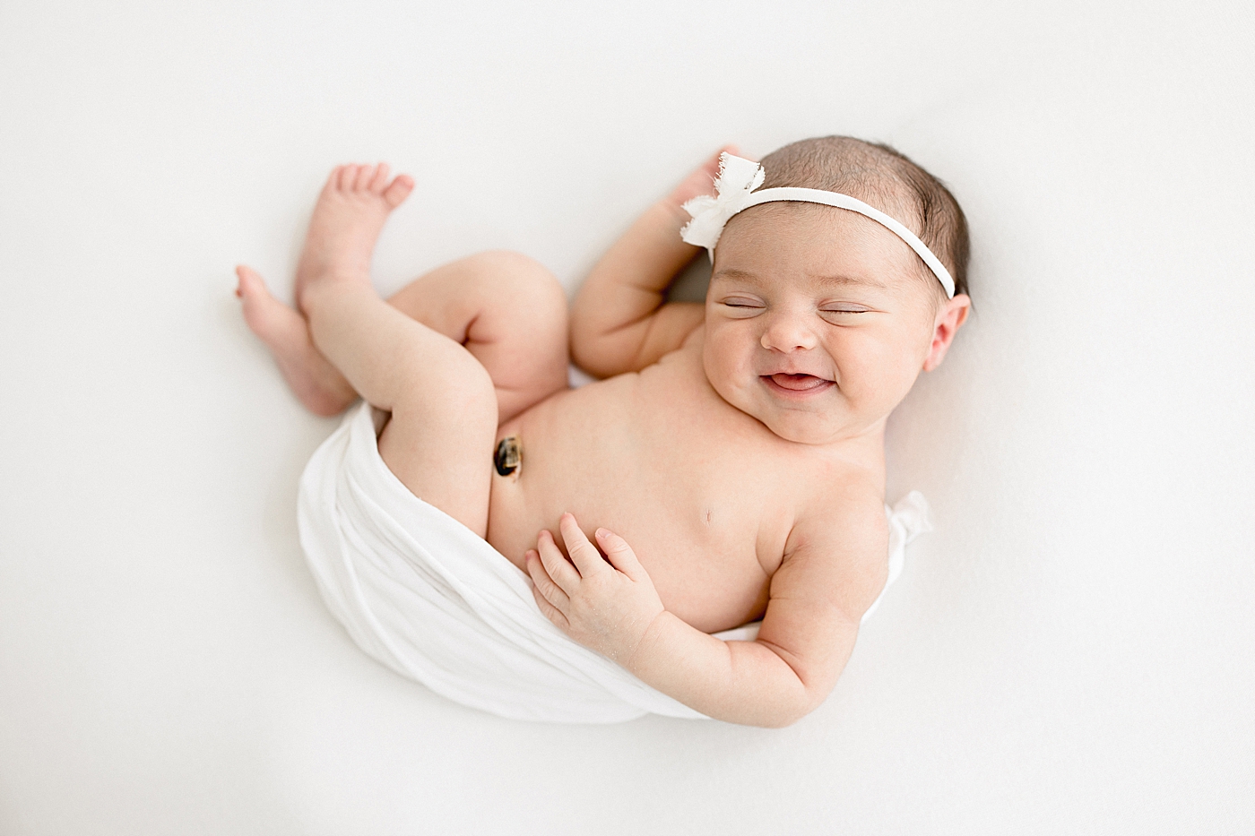 Newborn baby girl swaddled on her back and smiling. Photo by Brittany Elise Photography.